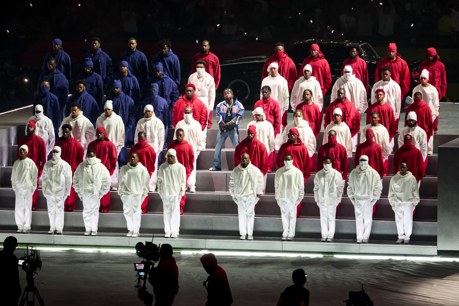 Kendrick Lamar występuje na Super Bowl, otoczony przez grupę artystów w kolorowych strojach.