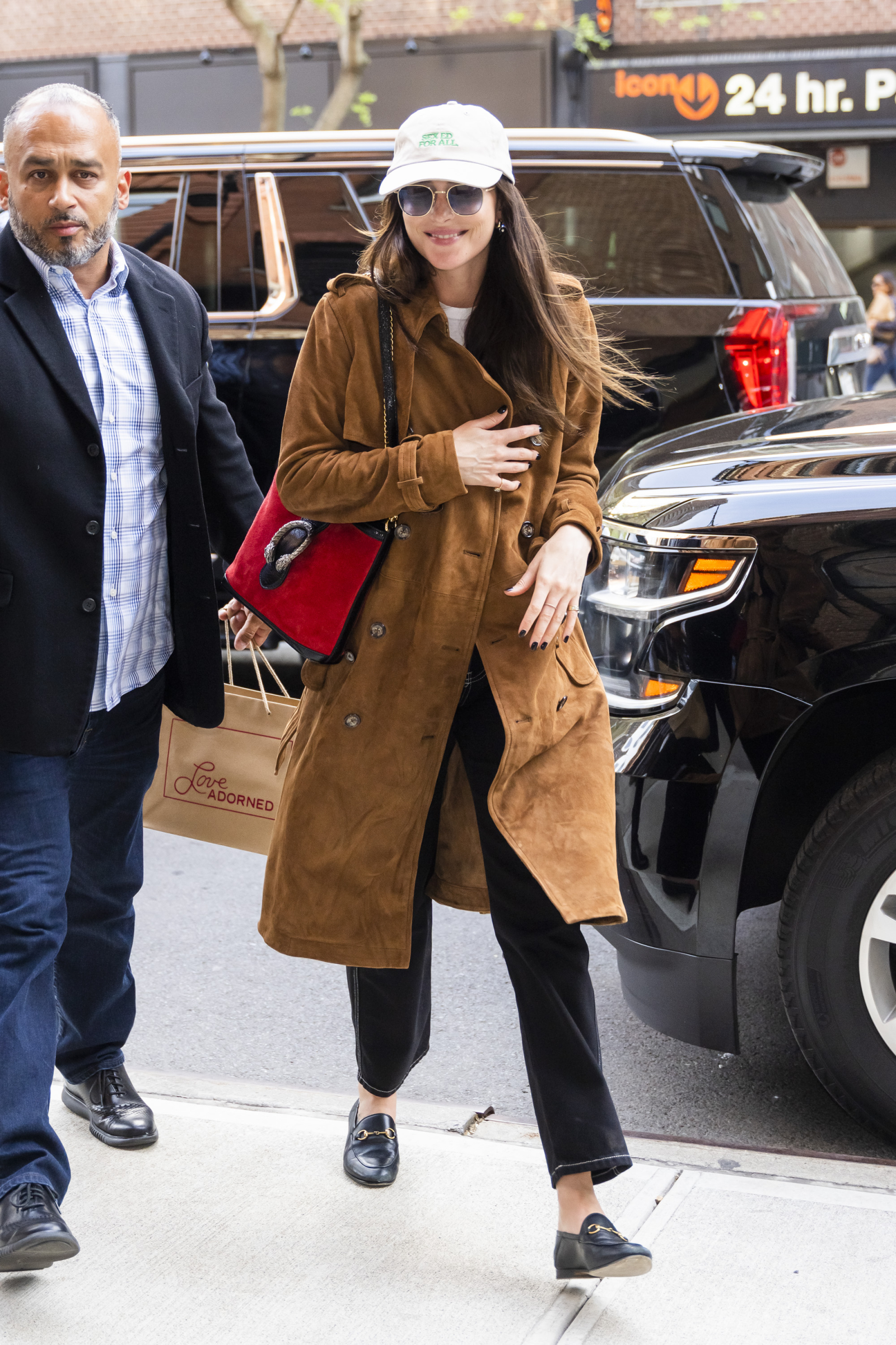 Dakota Johnson w modne mokasyny Gucci i brązowym płaszczu, spacerująca po mieście z towarzyszem.