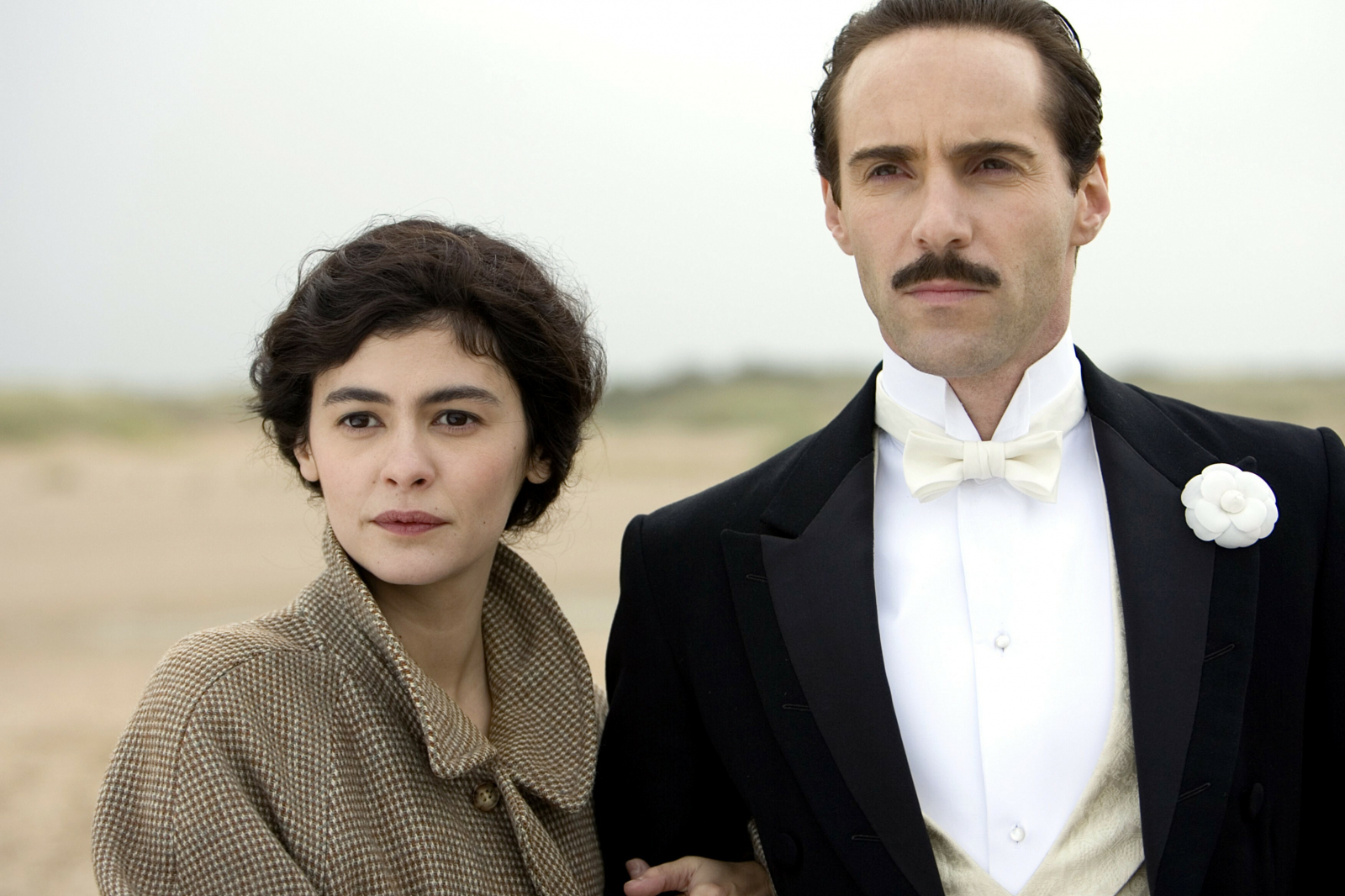 Coco Chanel i Boy Capel w romantycznej scenie z filmu, stoją na plaży w eleganckich strojach.