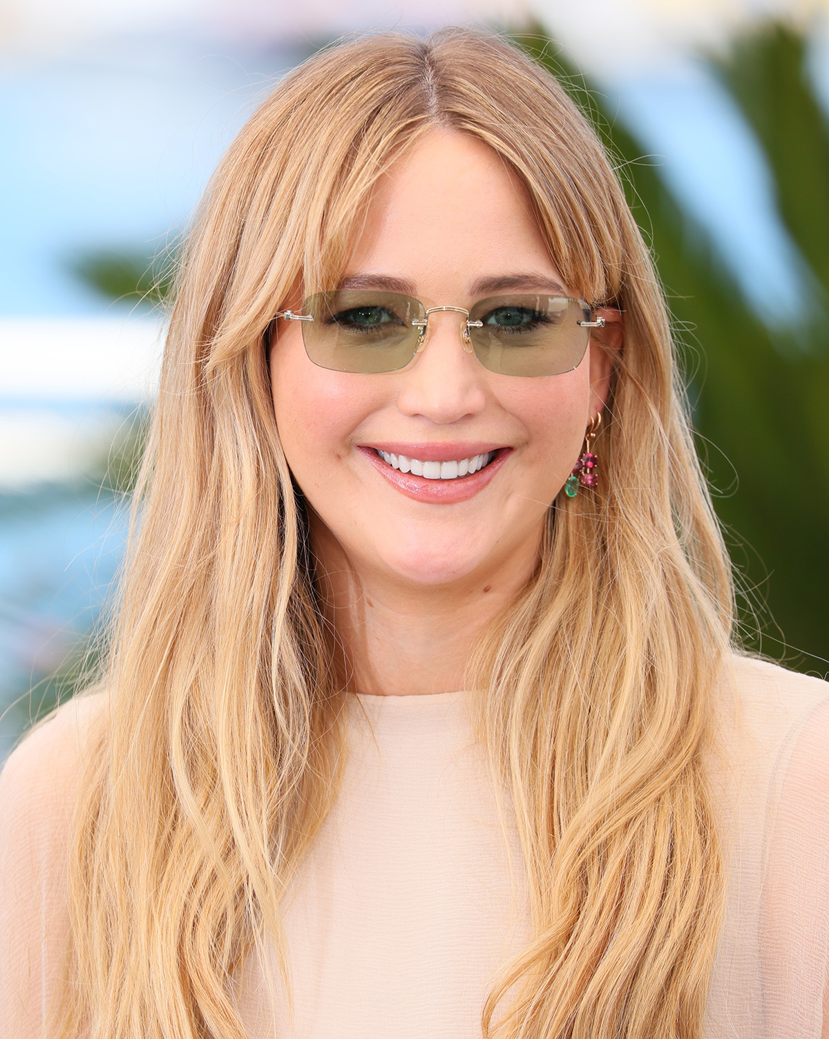 Jennifer Lawerence w brzoskwiniowej bluzce i okularach przeciwsłonecznych z zielonymi szkłami.