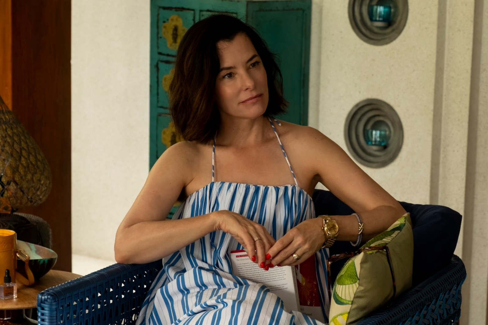 Parker Posey trzyma książkę, relaksując się w trzecim sezonie serialu „Biały Lotos”, w letniej sukience.