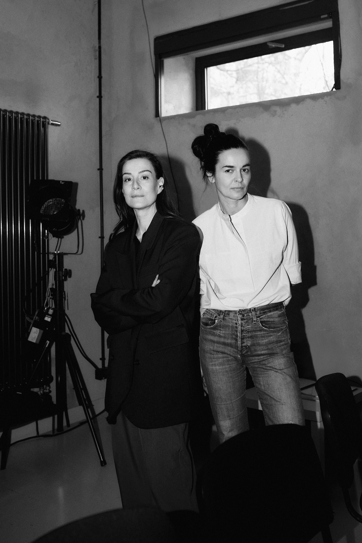 Maja Ostaszewska i Katarzyna Kalwat pozują w minimalistycznej scenerii, z oświetleniem filmowym w tle.