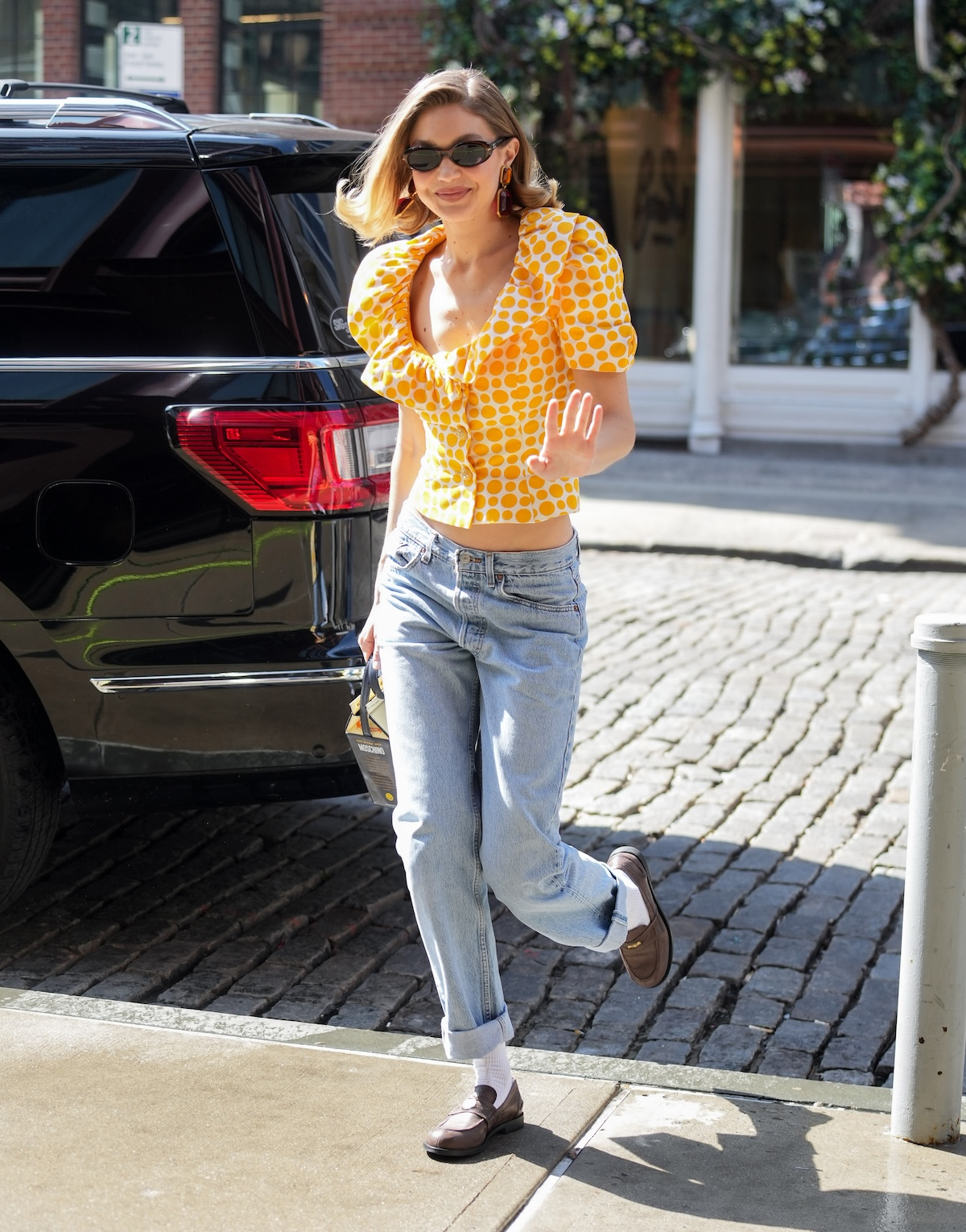 Gigi Hadid w żółtej bluzce w kropki, dżinsowych spodniach z podwiniętymi nogawkami i eleganckich butach.