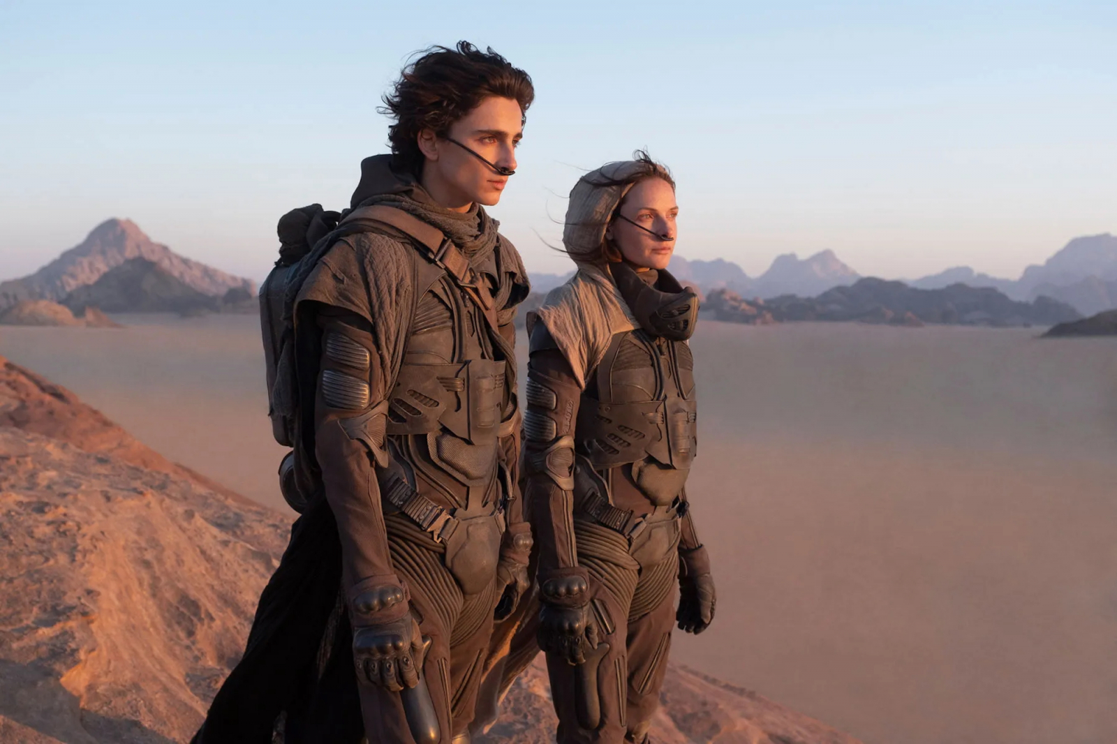 Timothée Chalamet i Rebecca Ferguson w filmie „Diuna” stoją na pustyni, patrząc w dal na majestatyczne góry.
