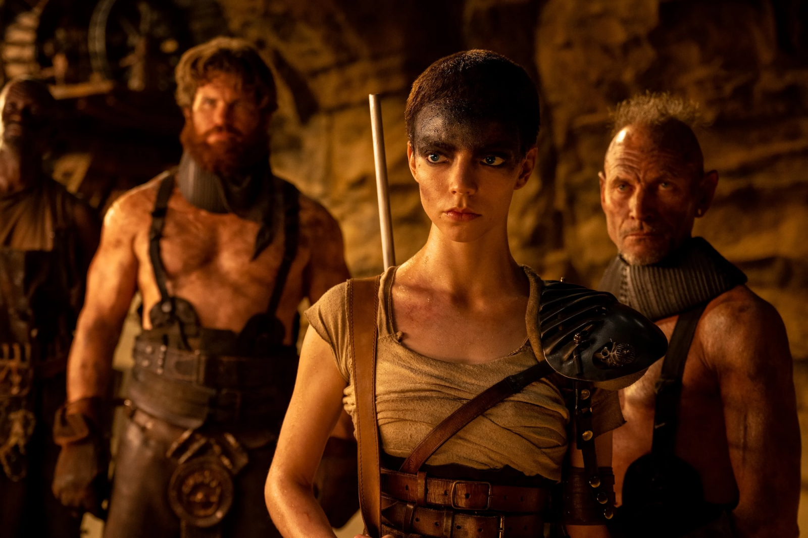 Anya Taylor-Joy w filmie „Furiosa: Saga Mad Max” w towarzystwie innych postaci w mrocznym, postapokaliptycznym otoczeniu.
