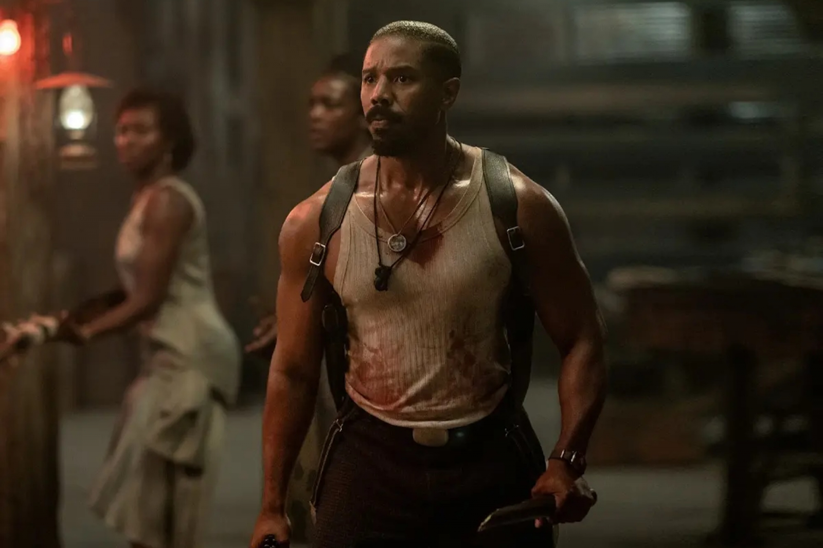 Michael B. Jordan w filmie „Grzesznicy”, ubrany w zniszczoną koszulkę, trzyma nóż, wygląda na zdeterminowanego.
