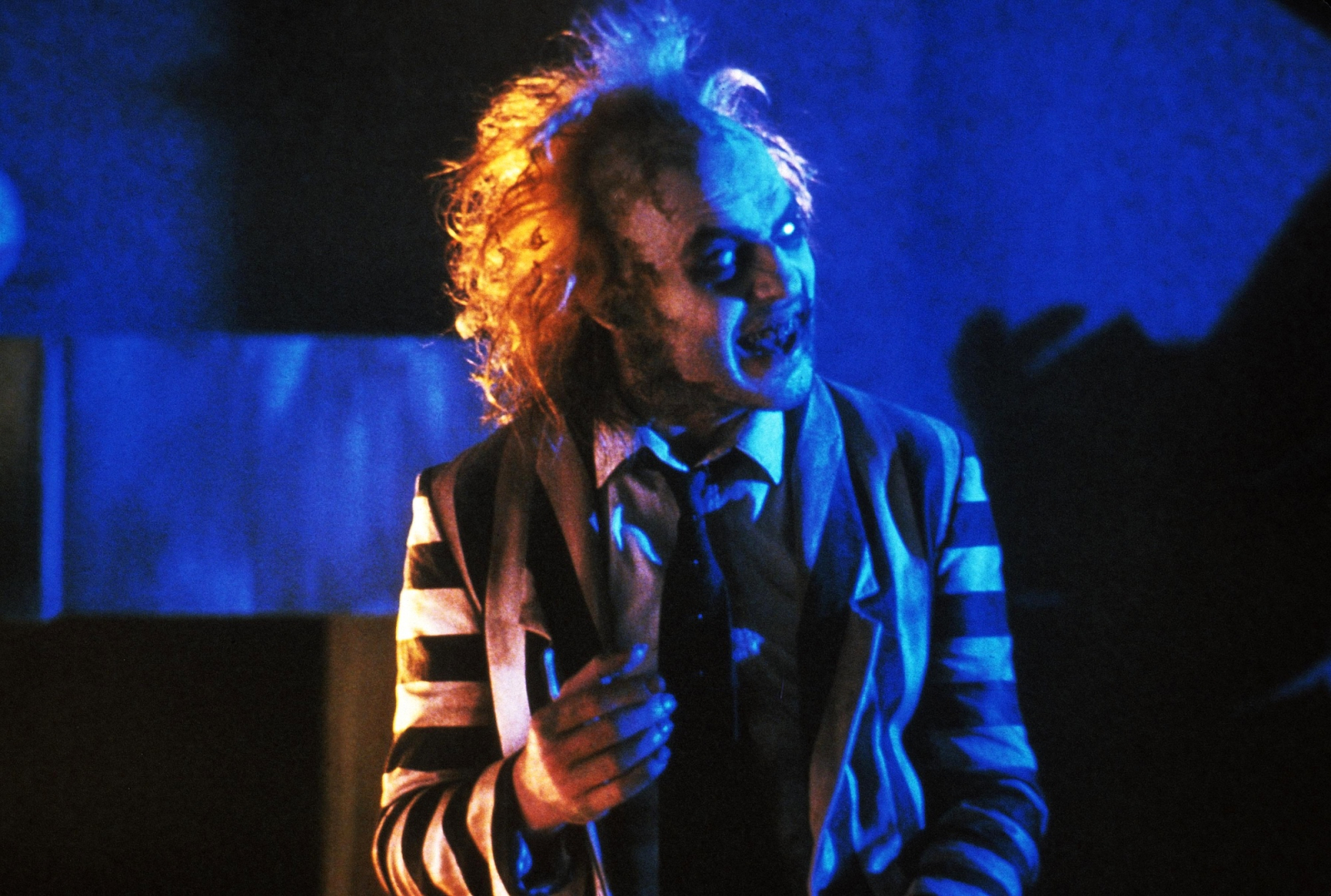 Michael Keaton jako Beetlejuice w kadrze z czarnej komedii „Sok z żuka”, z charakterystycznym makijażem i pasiastego garniturze.