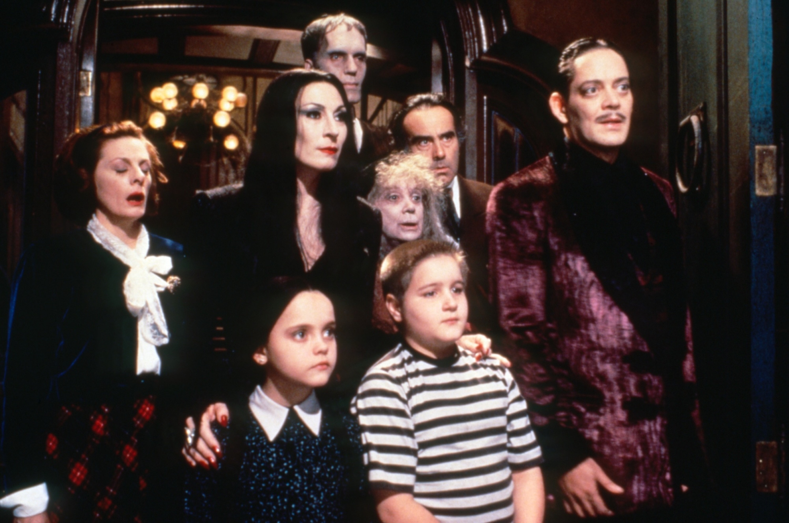 Rodzina w typowej dla siebie scenerii, z kultowej czarnej komedii „Rodzina Addamsów”, prezentująca swojski klimat.
