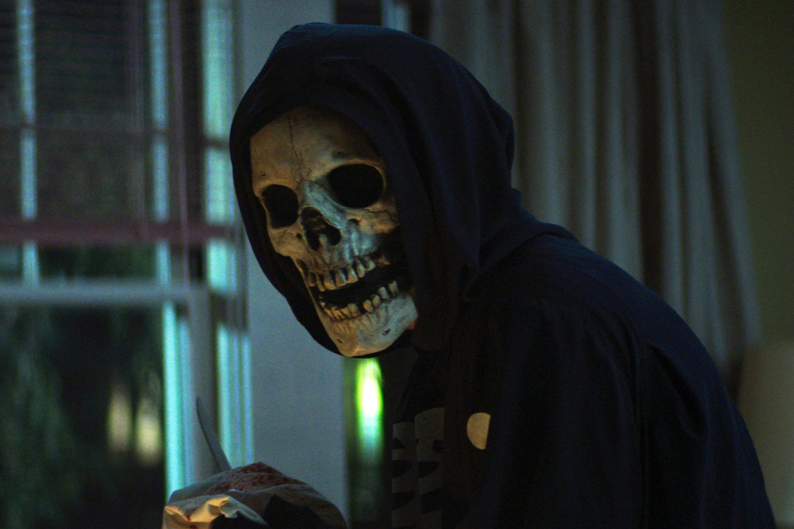 Ciemny kadr z horroru Netflix „Ulica Strachu”, przedstawiający postać w masce czaszki stojącą w mrocznym wnętrzu.