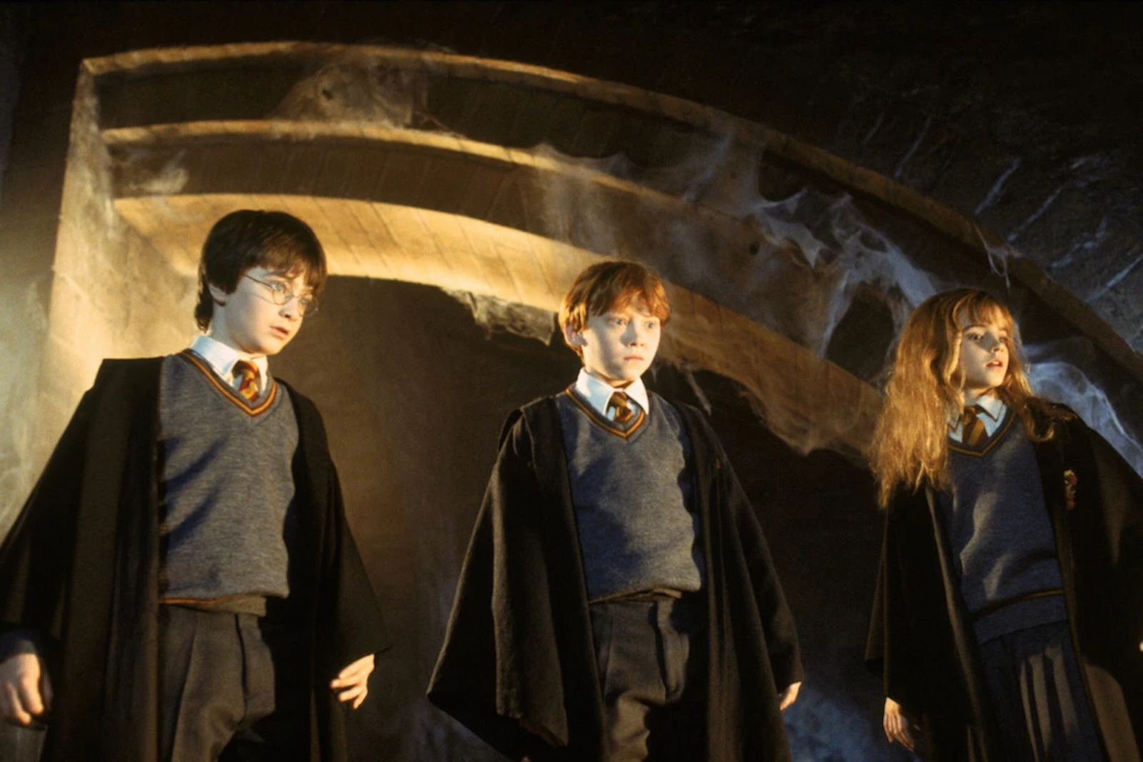 Ruppert Grint, Daniel Radcliffe i Emma Watson w filmie „Harry Potter i Kamień Filozoficzny” stoją w tajemniczej scenerii.