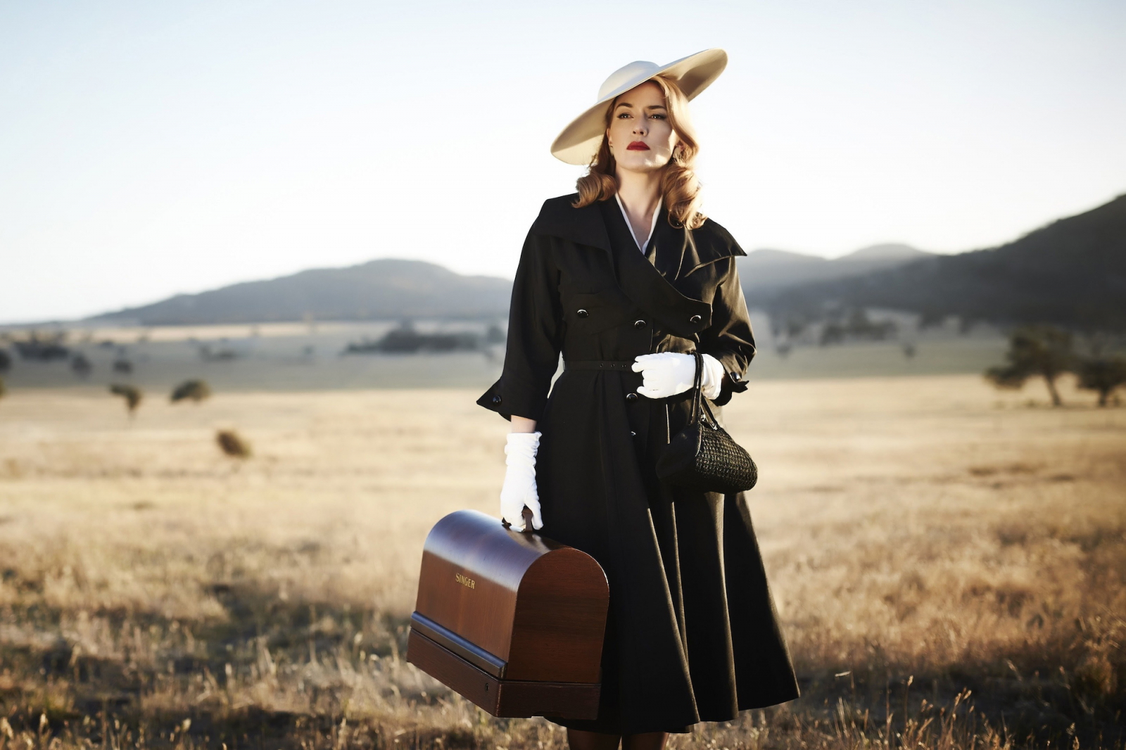 Kate Winslet jako Tilly Dunnage, film „Projektantka”, reżyseria Jocelyn Moorhouse, 2015 rok, w eleganckim płaszczu na tle krajobrazu.