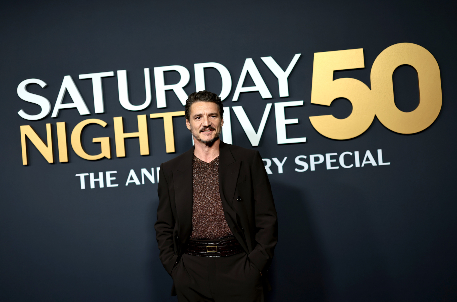 Pedro Pascal stoi w eleganckim stroju na tle napisu "SATURDAY NIGHT LIVE 50".