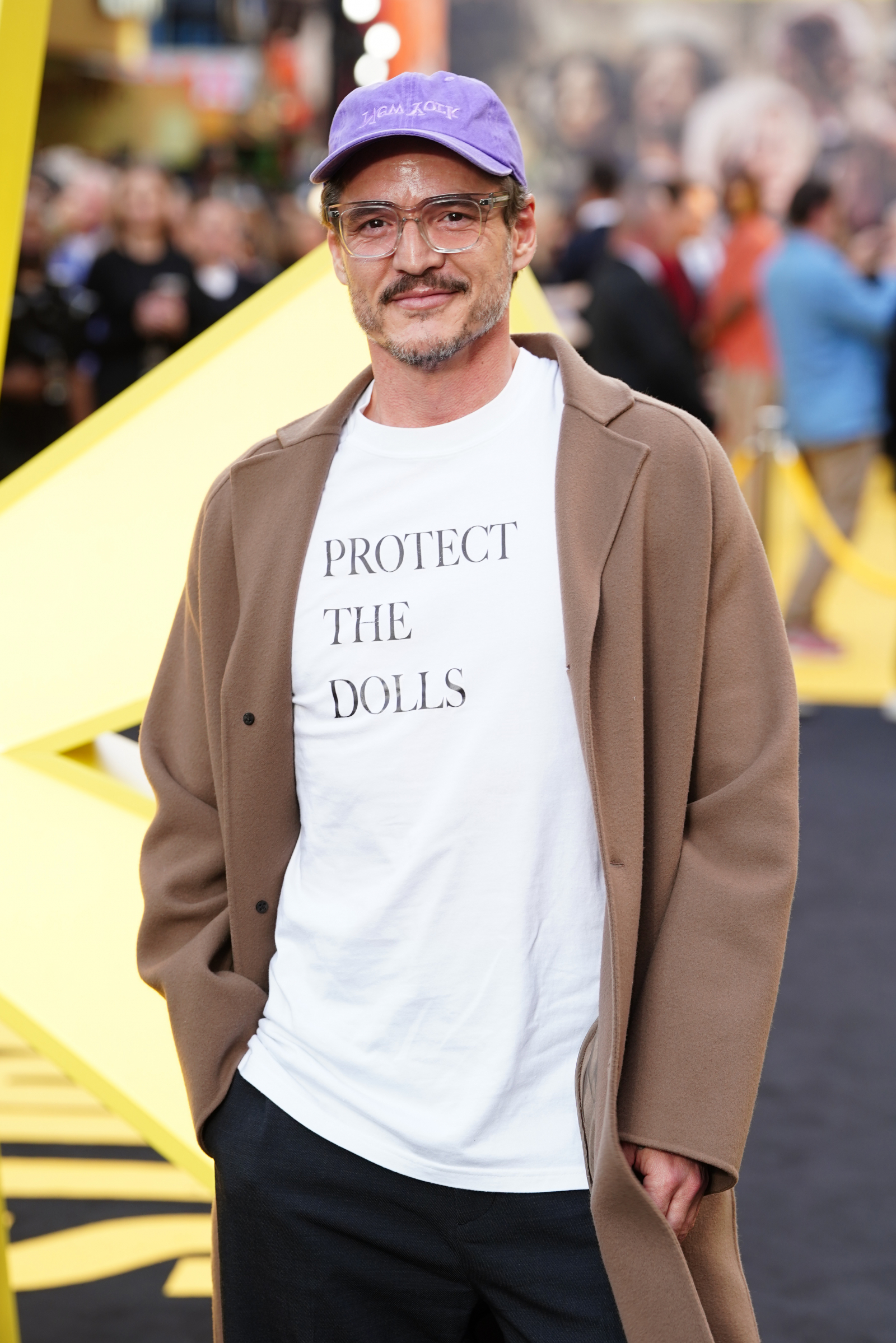 Pedro Pascal w beżowym płaszczu i białej koszulce z napisem "PROTECT THE DOLLS" na premierze filmu.