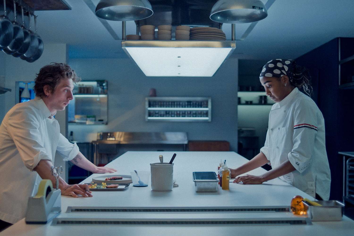 Jeremy Allen White i Ayo Edebiri w nowoczesnej kuchni, omawiając przygotowanie potraw.