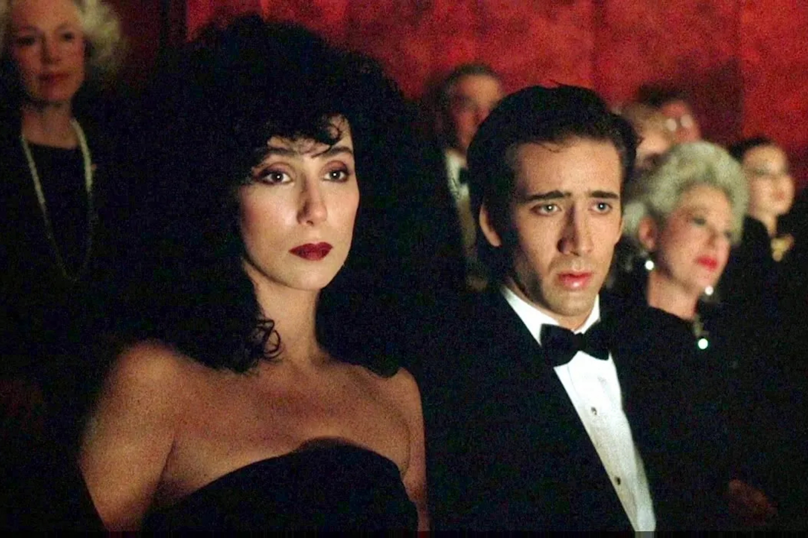 Cher i Nicholas Cage w filmie „Wpływ księżyca”, z wyrazami emocji na widowni.