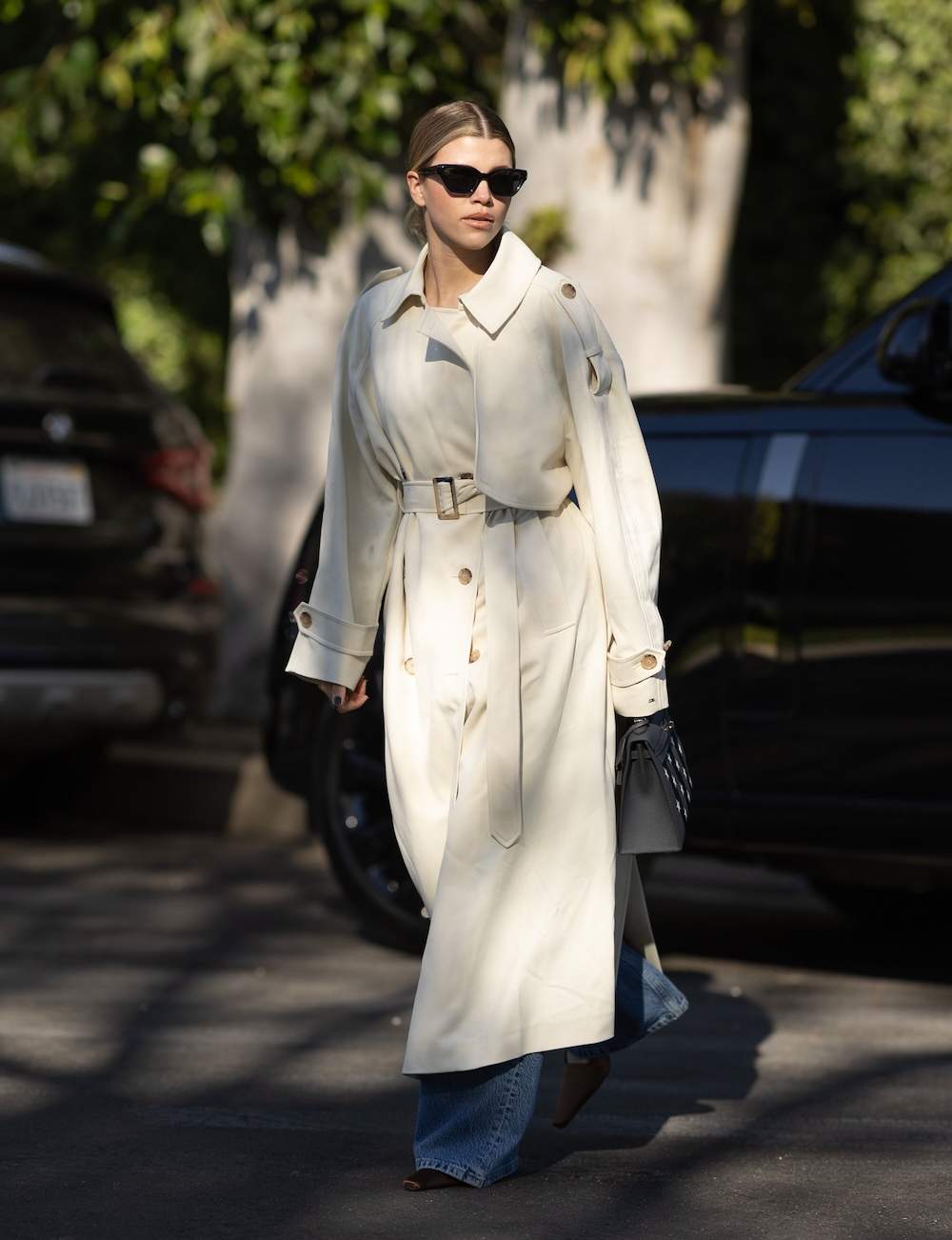 Sofia Richie Grainge w beżowym trenczu damskim, niebieskich jeansach i okularach przeciwsłonecznych.