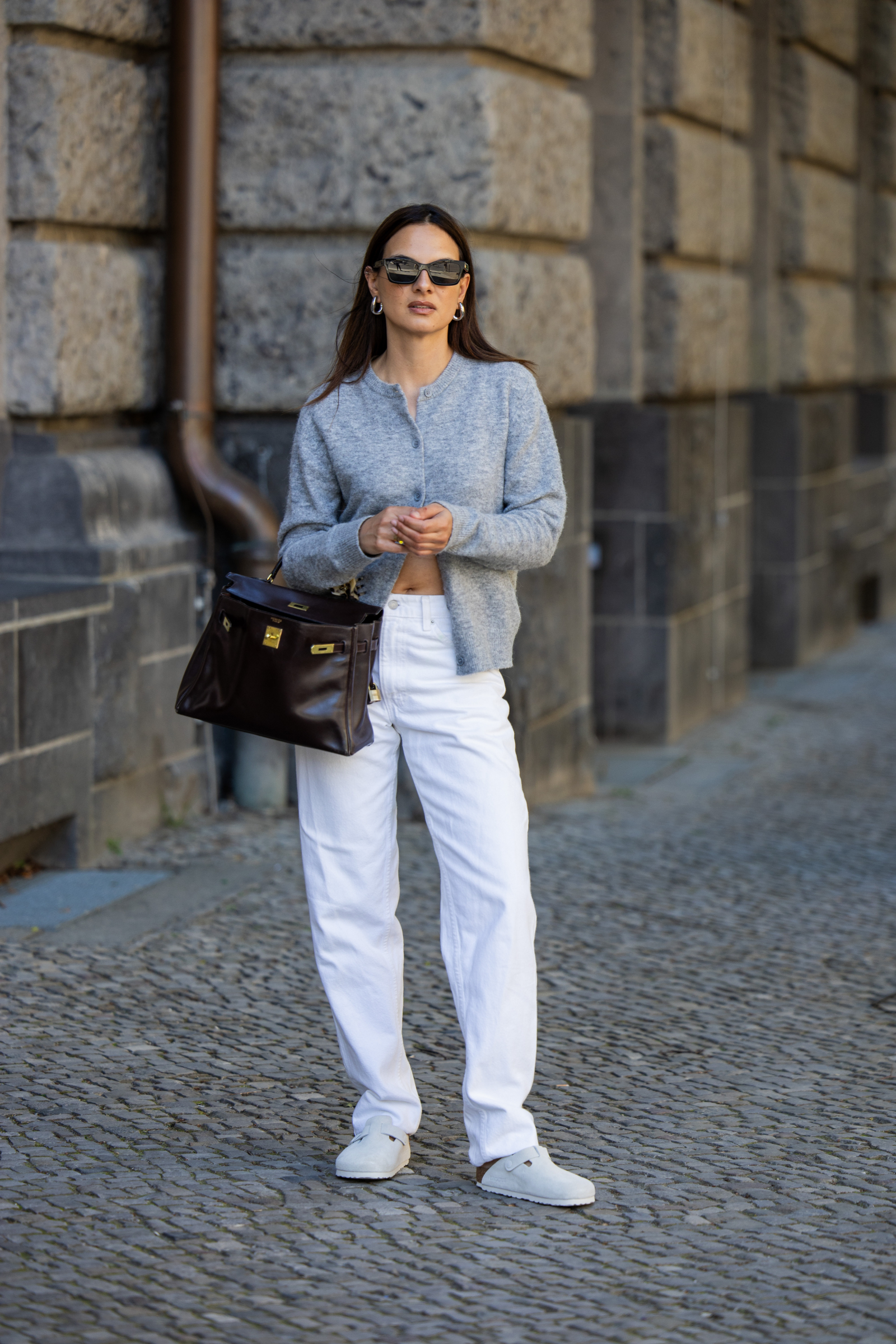 Jasne damskie klapki Birkenstock Boston w zestawieniu z białymi spodniami i szarym swetrem, stylowa na ulicy.