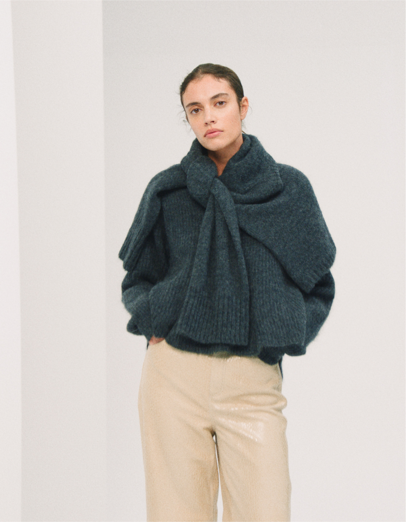 Kobieta w modnym swetrze damskim marki By Malene Birger, stylizowanym z dużym kołnierzem, w otoczeniu jasnych ścian.