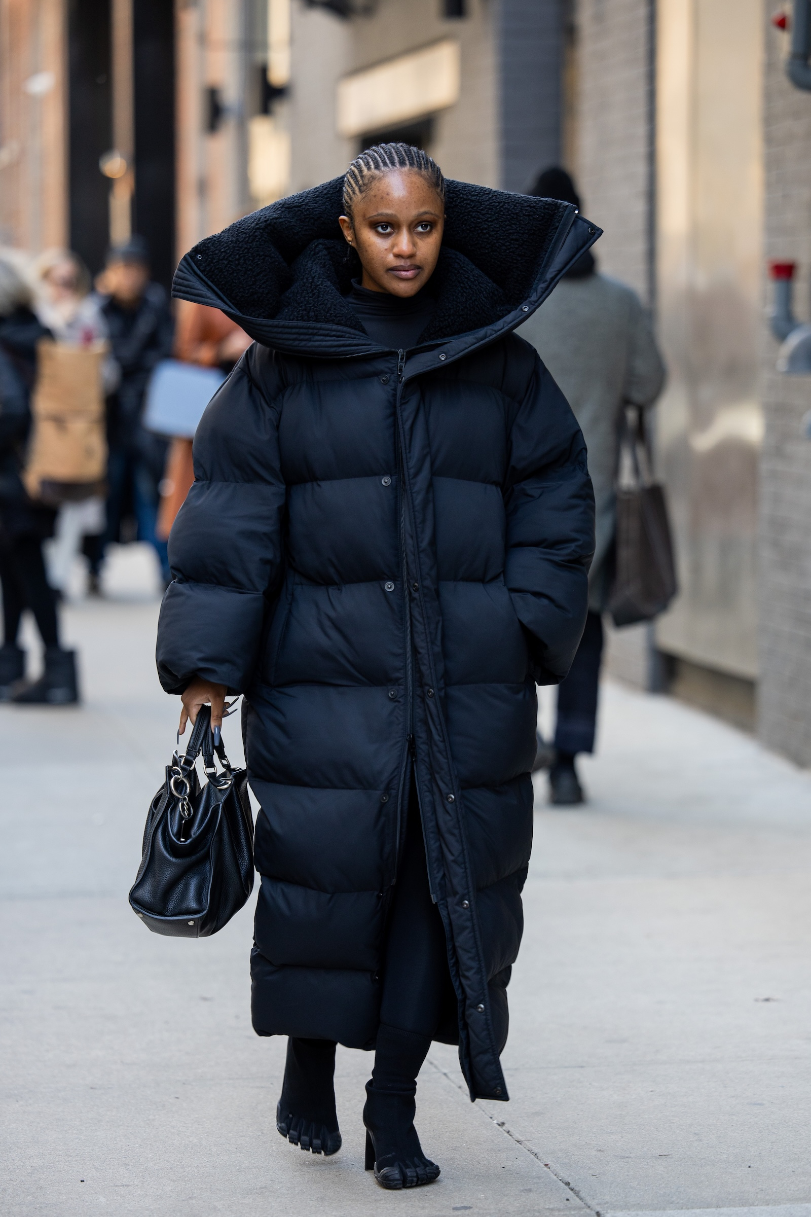Długa puchowa czarna kurtka damska z dużym kołnierzem, stylowy dodatek torebka w ręku, spacer po ulicy.