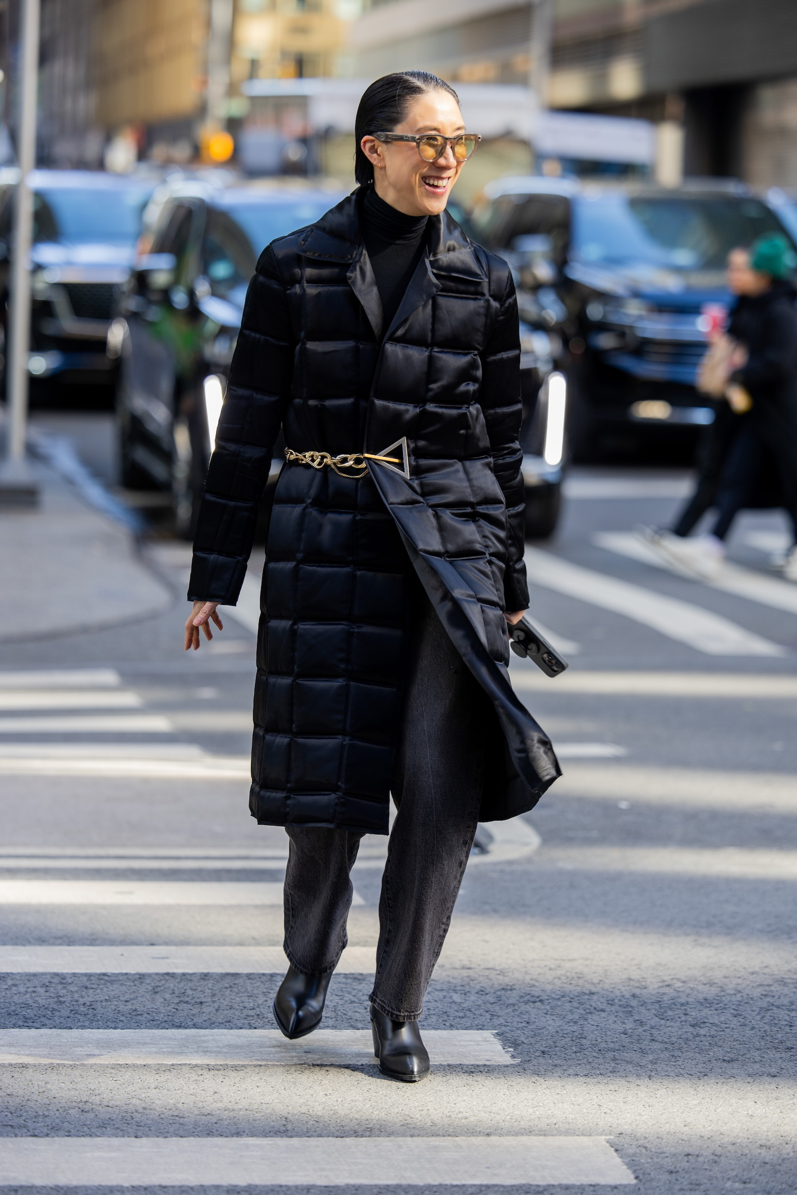 Eva Chen w długiej pikowanej czarnej kurtce, szarych jeansach barrel z wysokim stanem i czarnych botkach damskich.