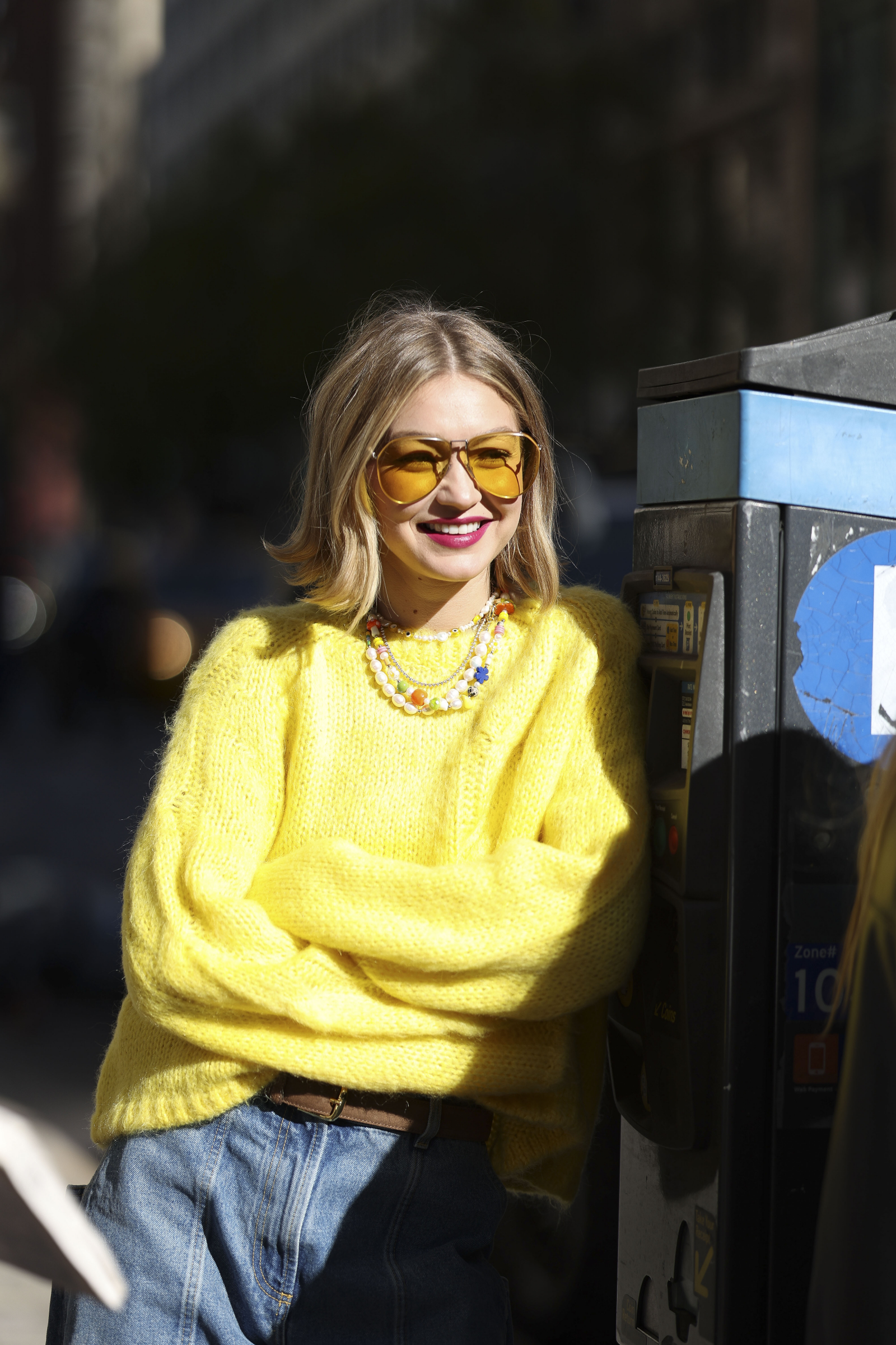 Gigi Hadid w żółtej, oversize’owej bluzie i żółtych okularach przeciwsłonecznych typu awiator.