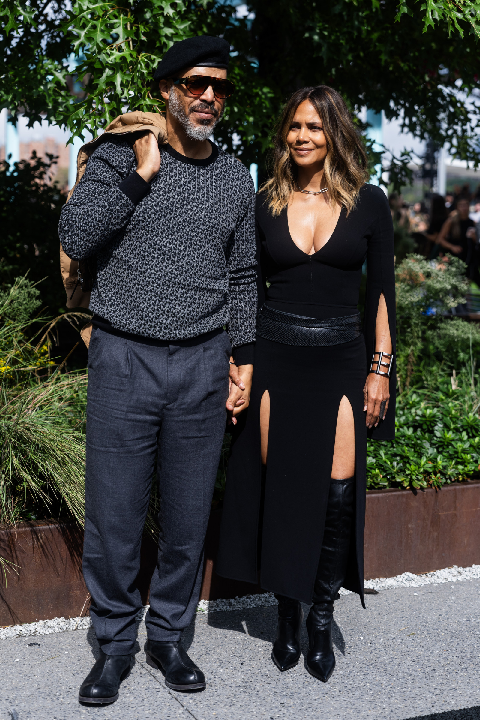 Halle Berry i Van Hunt trzymają się za ręce, pozując w eleganckich ubraniach w otoczeniu zieleni.