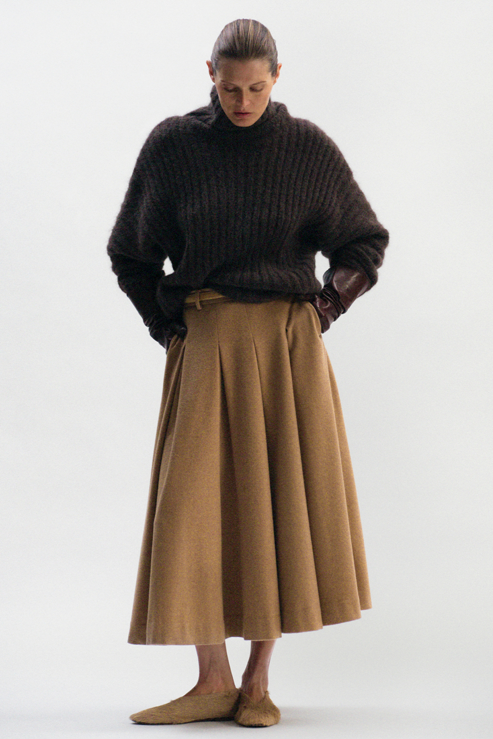 Małgosia Bela w brązowym swetrze damskim marki By Malene Birger, w eleganckiej, plisowanej spódnicy.