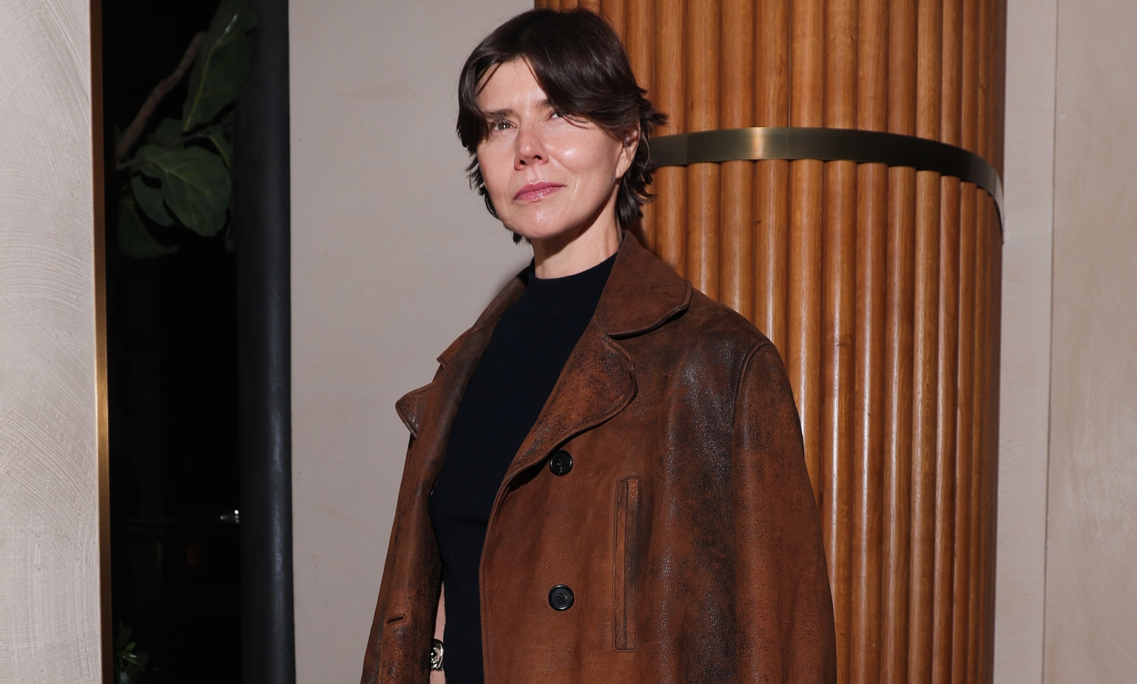 Małgorzata Szumowska na pokazie Miu Miu na sezon wiosna-lato 2026, w brązowej kurtce, pozująca na tle drewnianej ściany.