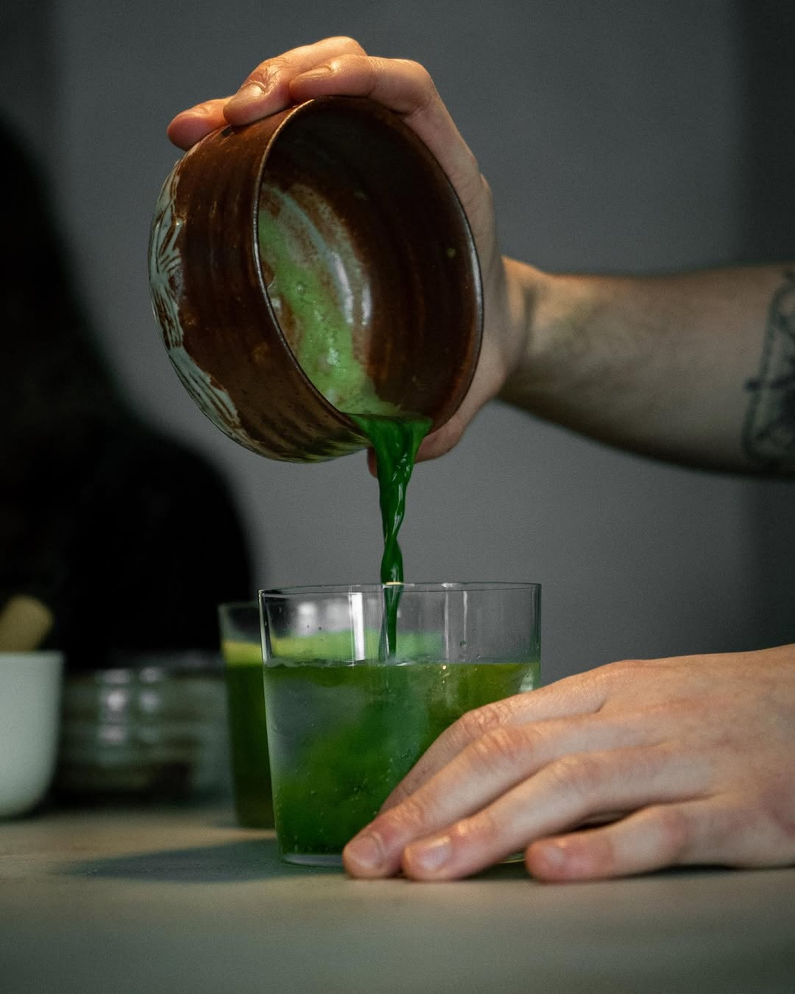 Osoba przygotowuje napój z matcha w kawiarni Happa to Mame, nalewając zielony płyn do szklanki.