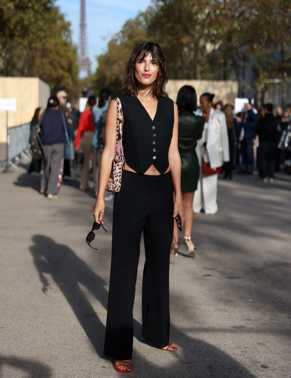 Jeanne Damas z modną torebką damską, pozująca w Paryżu na ulicy z wieżą Eiffla w tle.