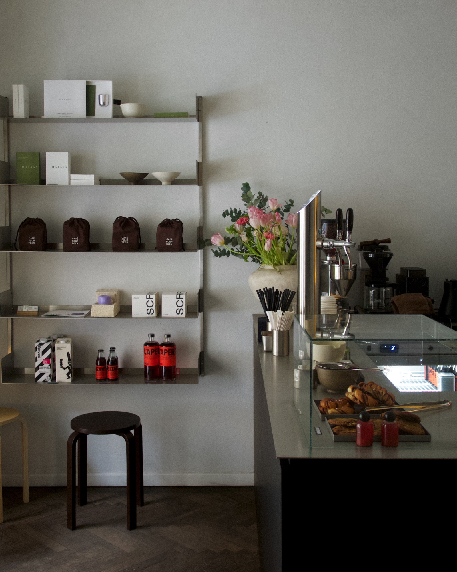 Wnętrze kawiarni Café Fourteen w Warszawie z regałem, kawą, kwiatami i wypiekami na ladzie.