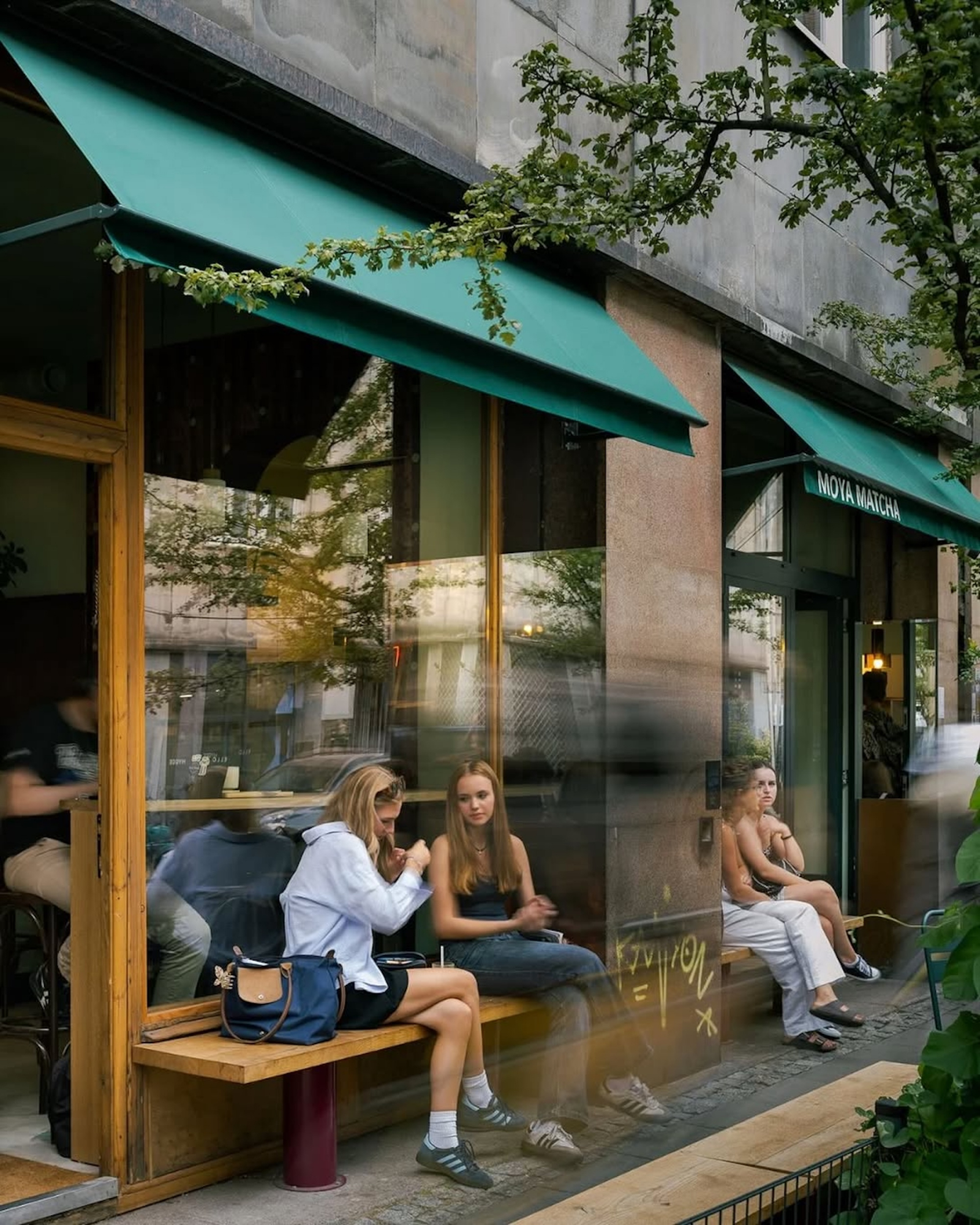 Kawiarnia Moya Matcha Bar w Warszawie, z widokiem na ludzi siedzących na ławce i przechodniów.