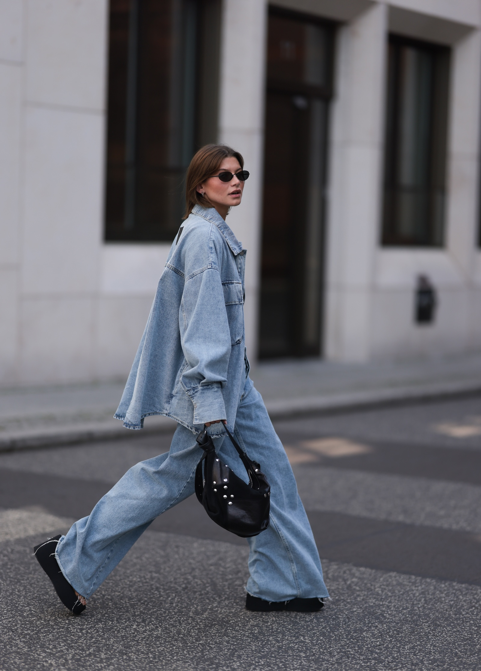 Modelka w jeansowej koszuli oversize i jeansach damskich baggy przechadza się po ulicy.