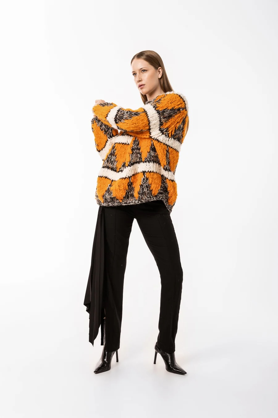 Damski sweter oversize Guðrun & Guðrun w kolorowe wzory, zestawiony z eleganckimi czarnymi spodniami.