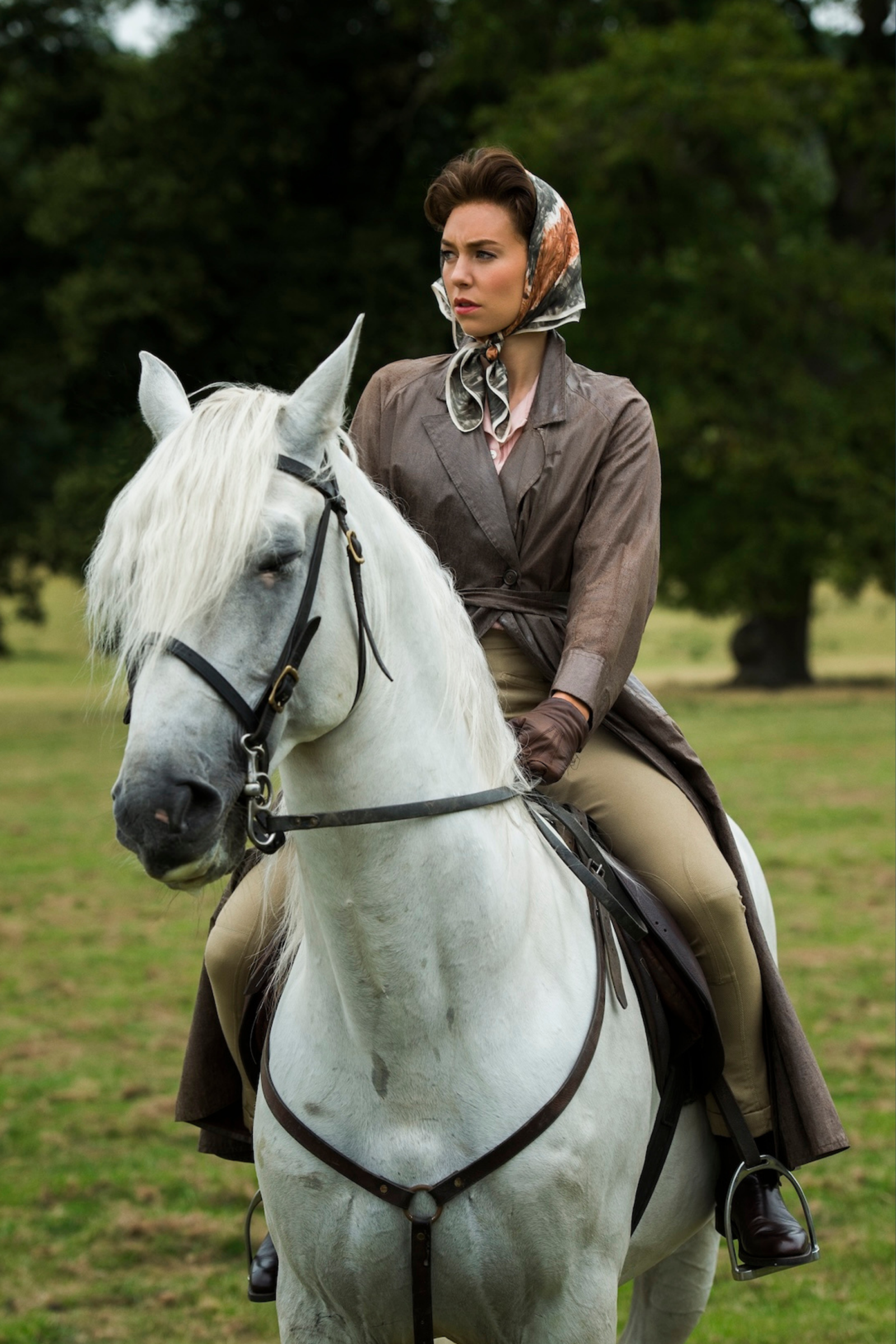 Vanessa Kirby w stroju jeździeckim na białym koniu, z serii Netflix „The Crown”. Tło to zielone pole i drzewa.
