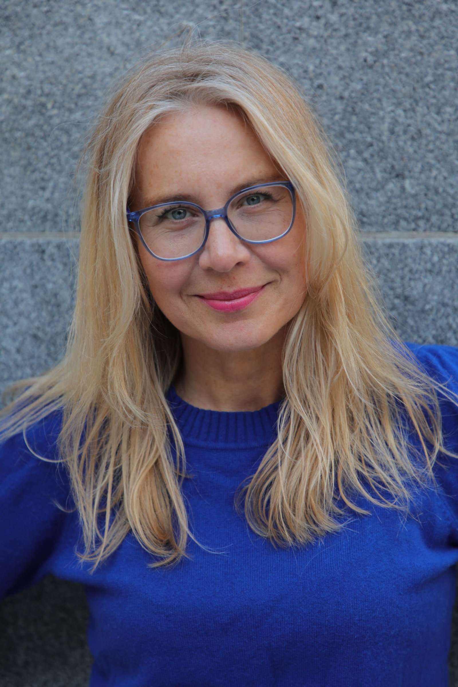 Astrid Wendlandt, założycielka niezależnego portalu Miss Tweed, uśmiecha się w niebieskim swetrze na tle szarej ściany.