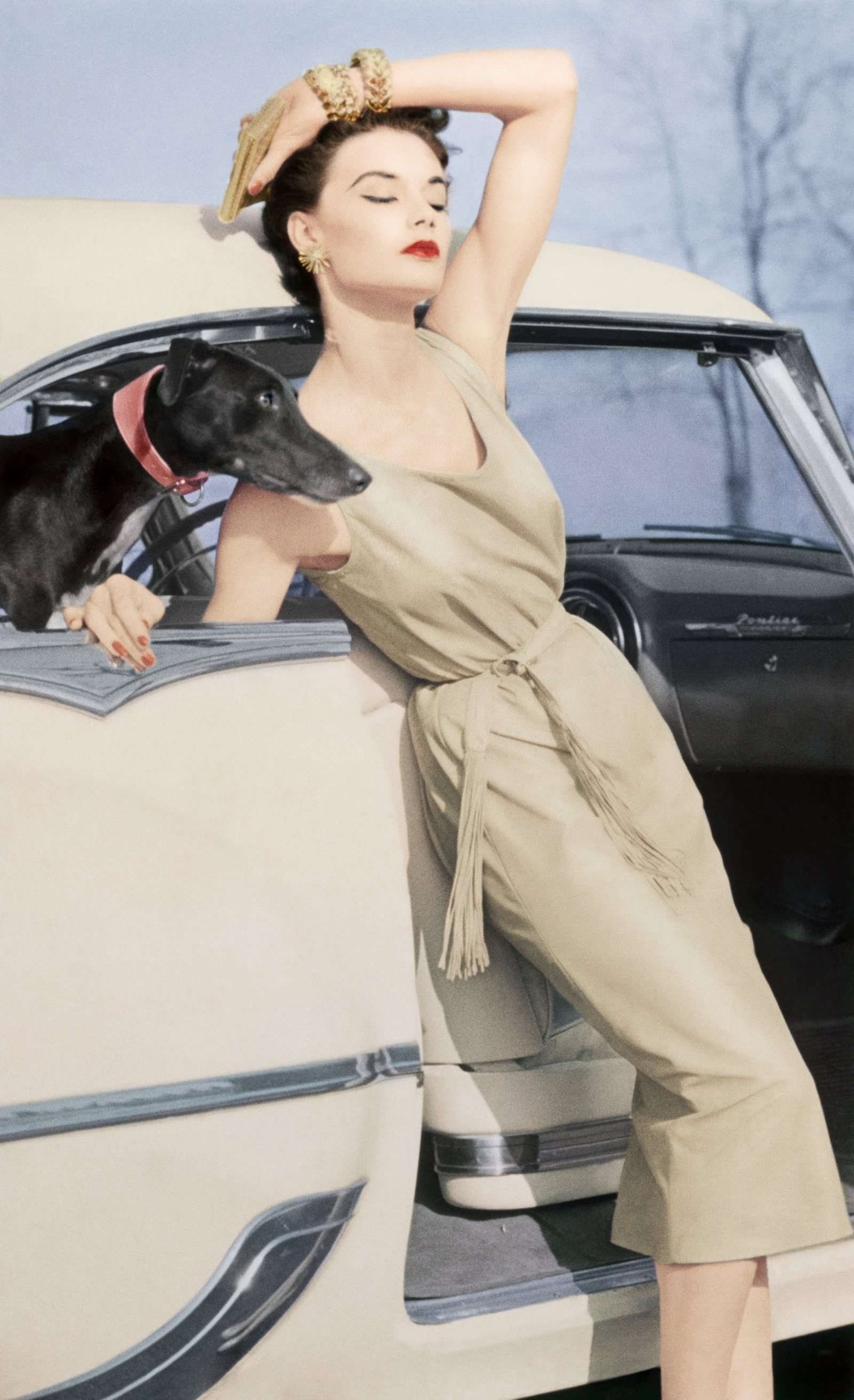Modelka w eleganckiej sukience z makijażem w stylu lat 50. w Vogue, 1954 rok, pozująca przy klasycznym samochodzie z psem.