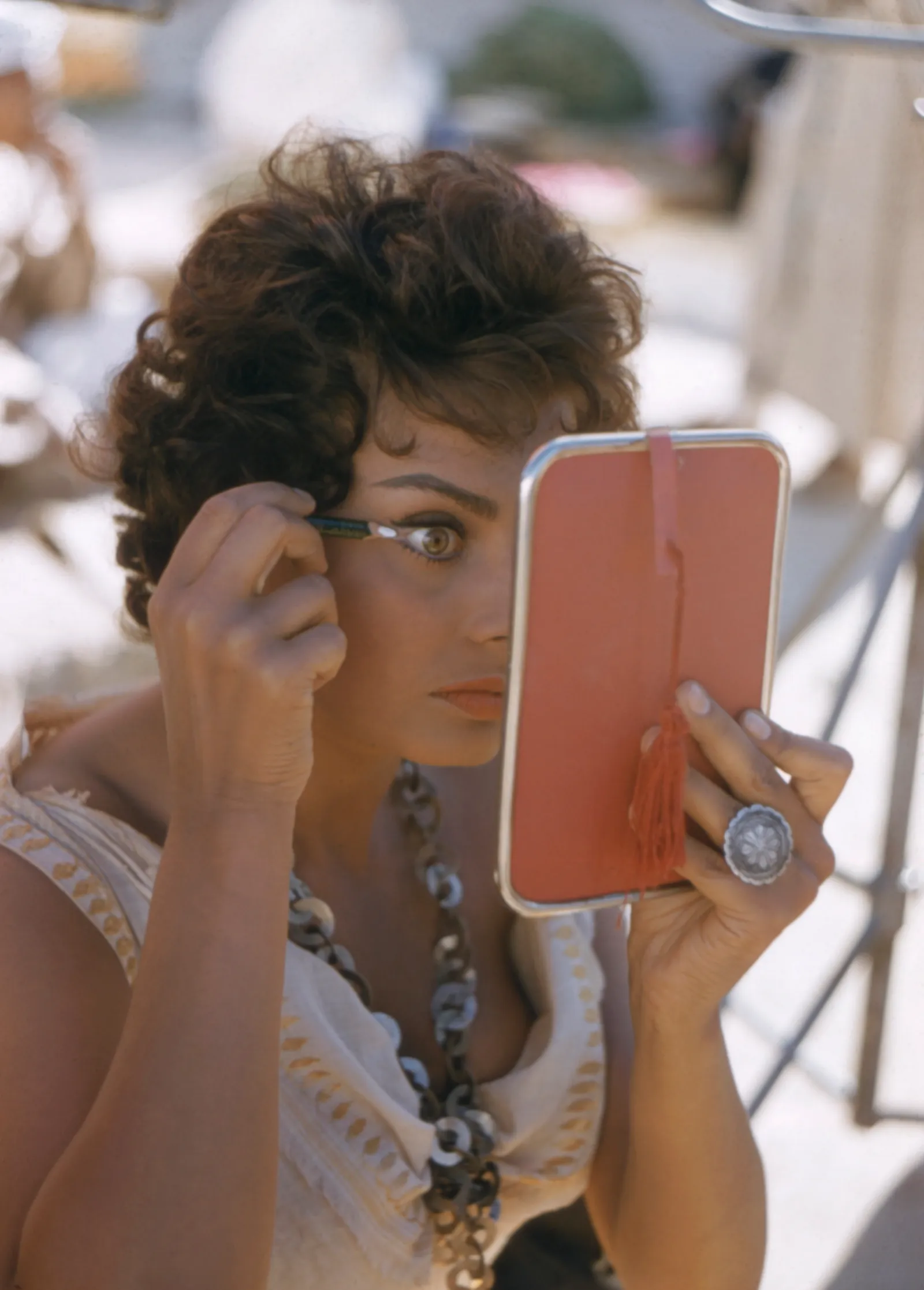 Sophia Loren wykonuje makijaż w 1957 roku, skupiona i elegancka, trzymając lusterko.