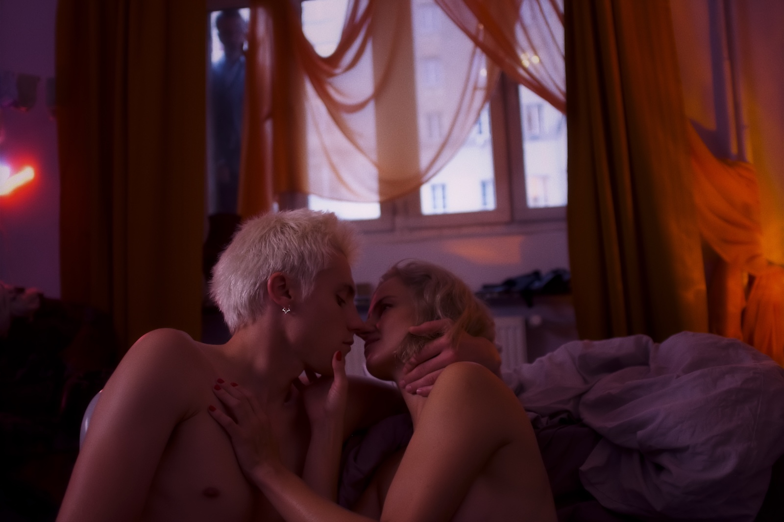 Kadr z filmu „Trzy miłości” przedstawia intymny moment dwojga ludzi w kolorowym, nastrojowym otoczeniu.