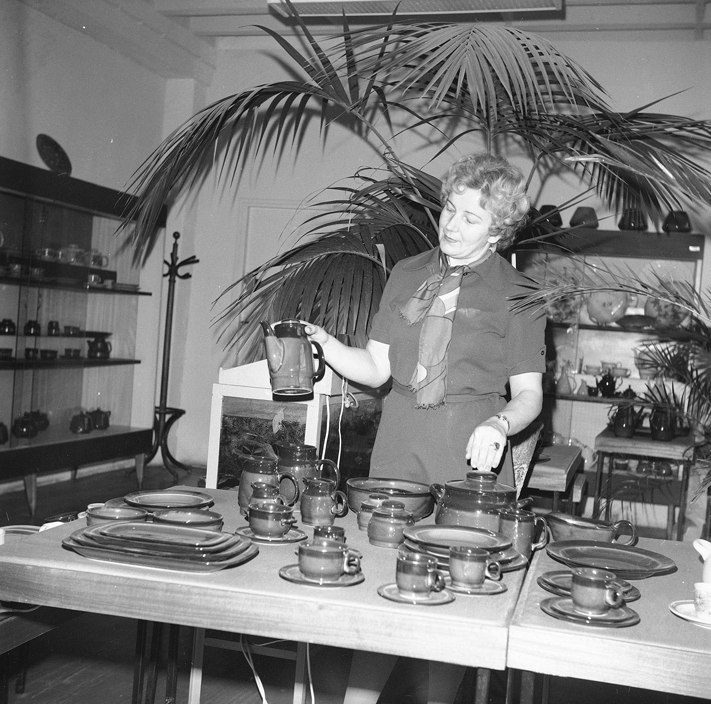 Kobieta przy wyprodukowanych filiżankach, talerzach i imbrykach. Zakłady Porcelitu Stołowego „Pruszków. Autor Rutowska Grażyna. Narodowe Archiwum Cyfrowe.