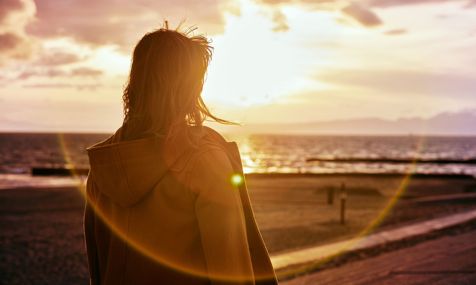 Kobieta na plaży na tle zachodzącego słońca (Fot. Getty Images)