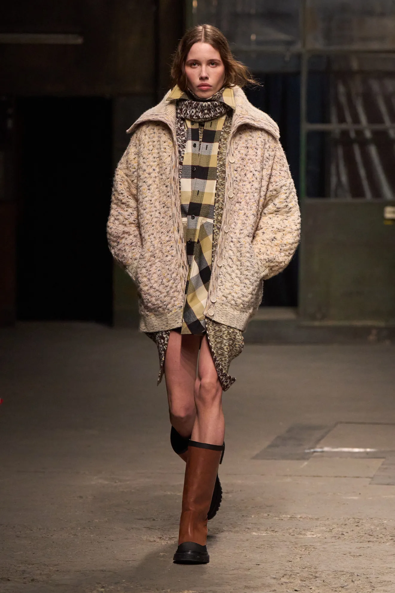 Modelka w trykocie i oversize'owym kardiganie, idzie po wybiegu, prezentując modną stylizację.