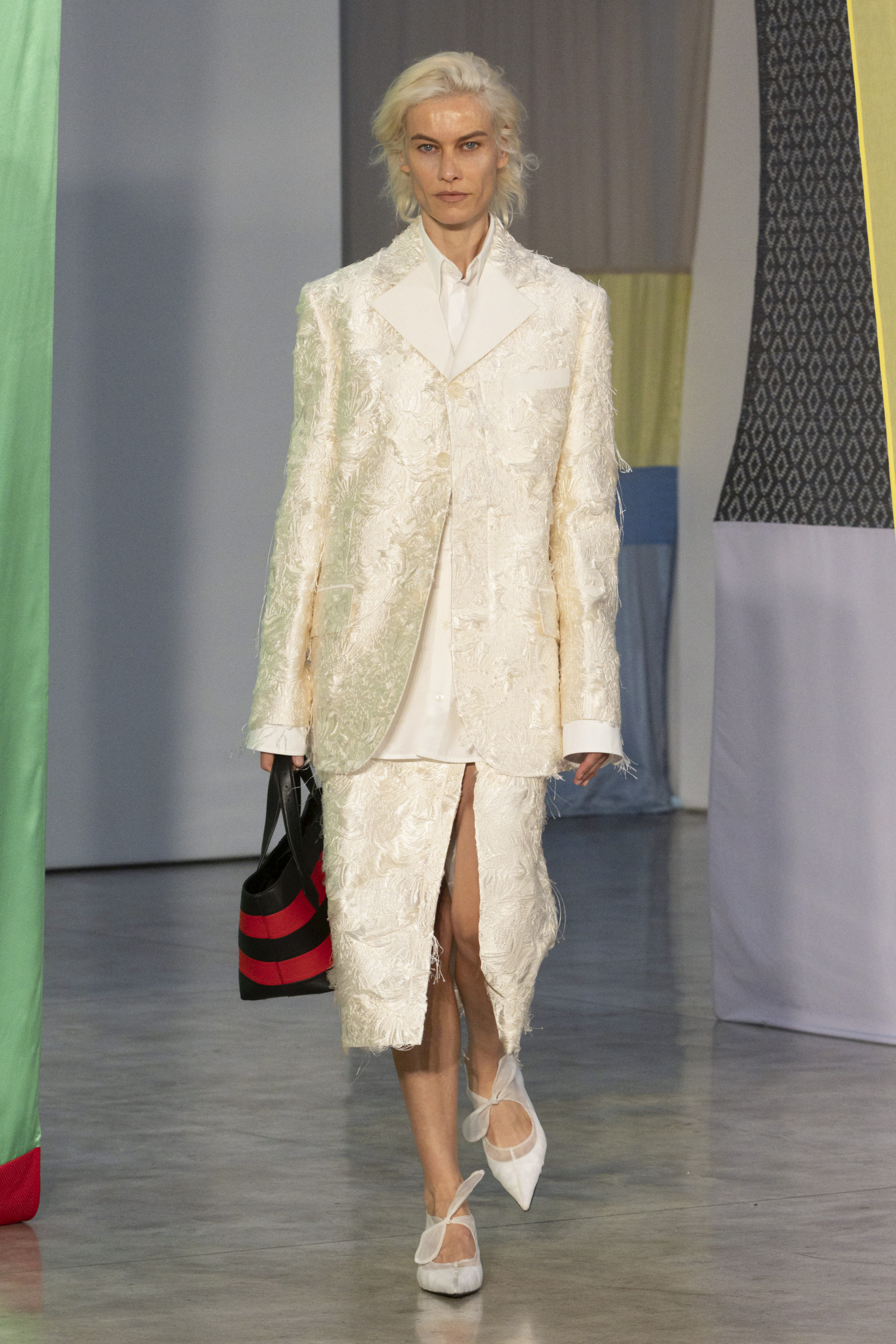 Modelka w eleganckim żakiecie Proenza Schouler, nosząca midi spódnicę i stylowe obuwie, prezentuje nową kolekcję.
