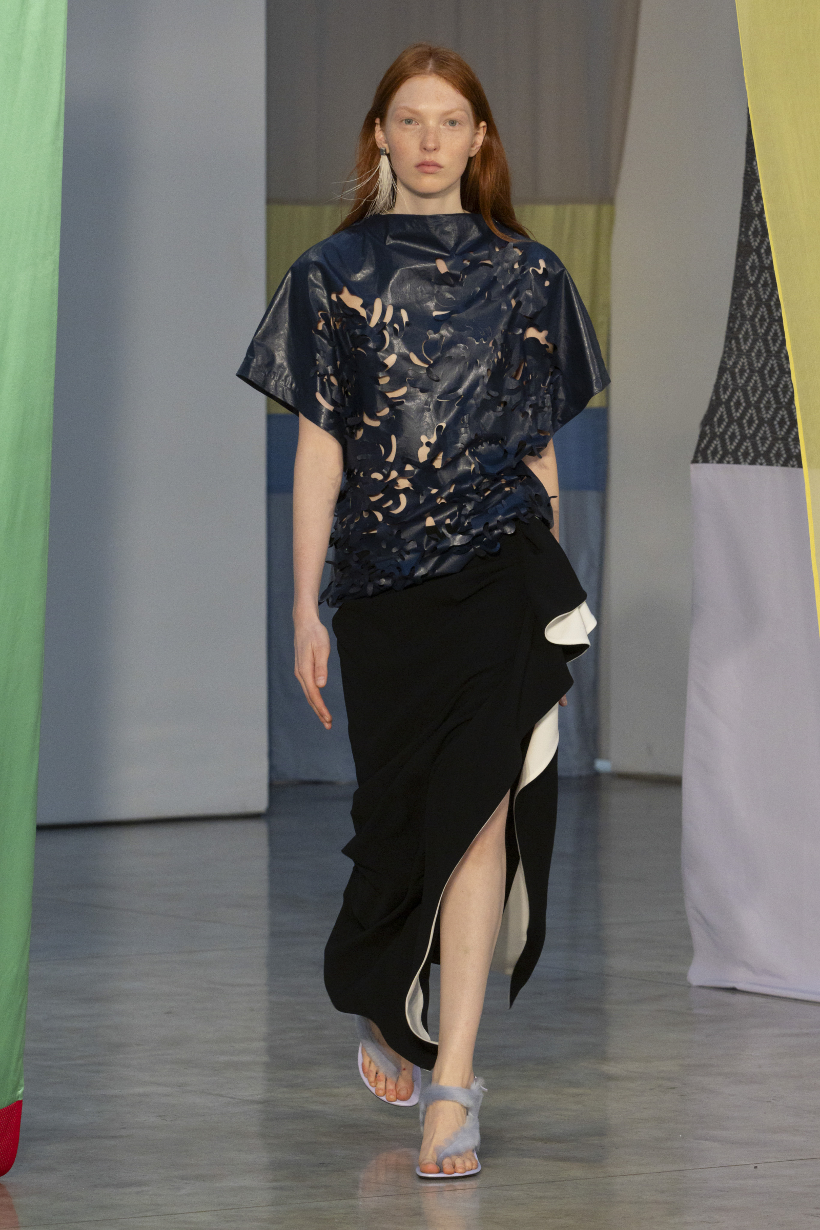 Modelka nosi asymetryczną spódnicę midi oraz skórzany top od Proenza Schouler, prezentując nowoczesny styl.