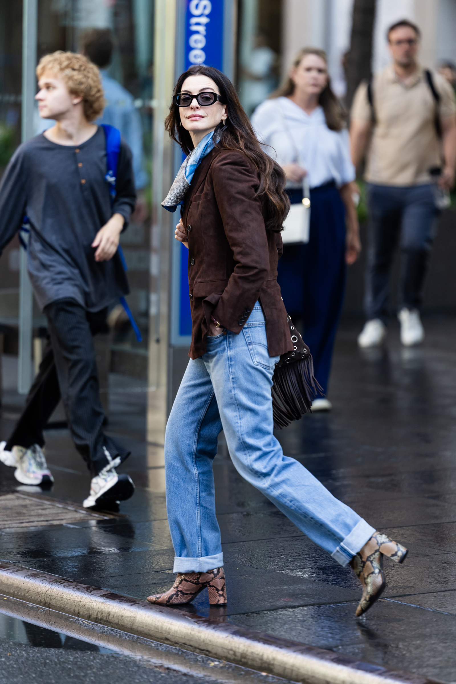 Anne Hathaway w brązowej marynarce i niebieskich jeansach z podwiniętymi nogawkami, w botkach w skórę węża na planie filmu „Diabeł ubiera się u Prady 2”.