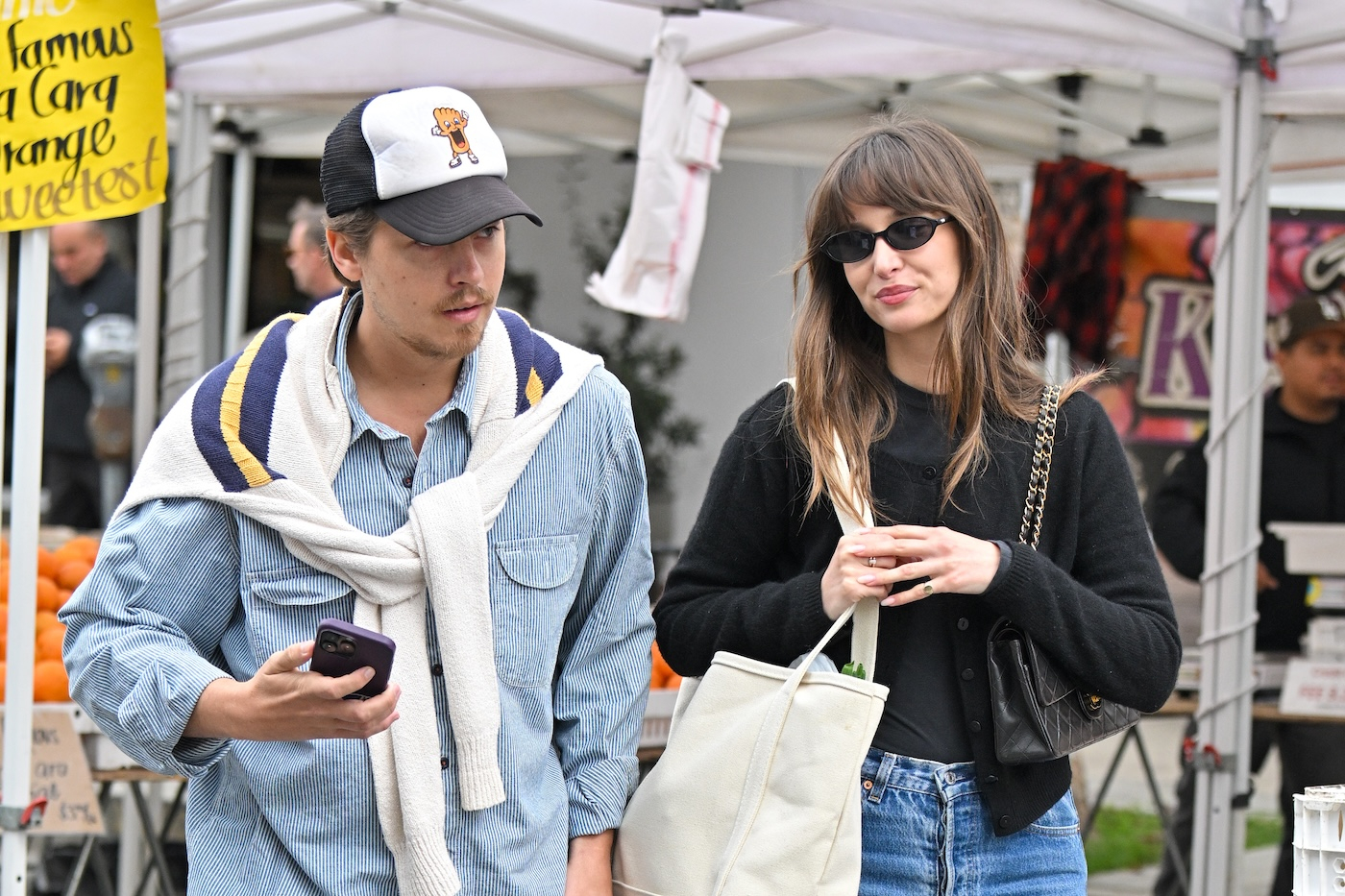 Cole Sprouse i Ari Fournier podczas zakupów spożywczych w Los Angeles, w Kalifornii, Cole Sprouse ma na sobie błękitną koszulę i zarzucony na ramiona biały sweter oraz czapkę z daszkiem, Ari Fournier ma na sobie czarny sweter, czarną torebkę Chanel i czarne okulary przeciwsłoneczne i białą torbę z zakupami.