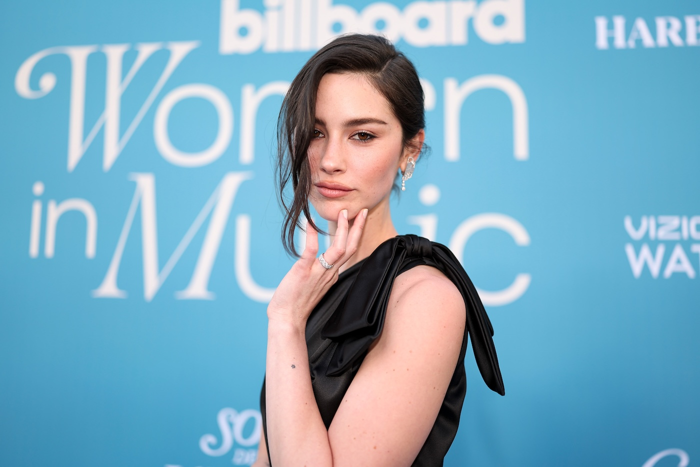 Gracie Abrams pozuje do zdjęcia podczas wydarzenia Billboard Women in Music Awards 2025, ma spięte włosy i nosi czarną sukienkę na jedno ramię.
