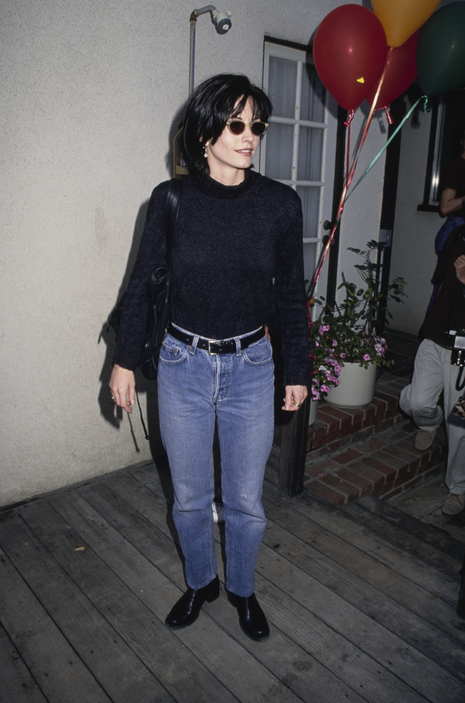 Courtney Cox w czarnym swetrze i jeansach damskich z 1995 roku na przyjęciu z balonami w tle.