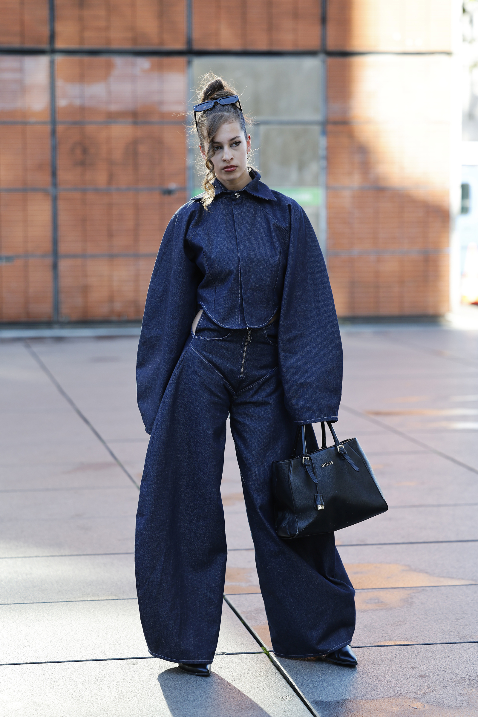 Modelka w jeansach barrel z wysokim stanem w kolorze indygo, nosi czarną torebkę i ma sprytne fryzury.