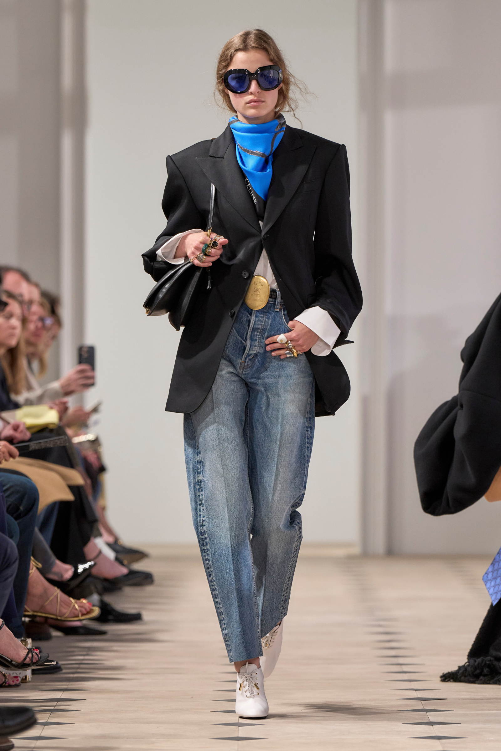 Modelka w retro stylizacji z dużymi okularami przeciwsłonecznymi, w jeansach barrel z wysokim stanem marki Celine i oversize'owym żakiecie.